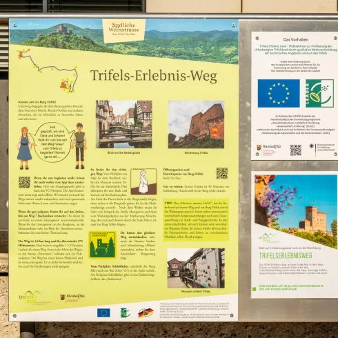 Informationstafel zum Trifels-Erlebnis-Weg mit einer Karte und historischen Informationen. Sie zeigt Sehenswürdigkeiten und Aktivitäten in der Umgebung.