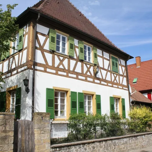 Ein wunderschönes, traditionelles Fachwerkhaus mit grünen Fensterläden. Es steht in einer malerischen Straße mit anderen charmanten Häusern.