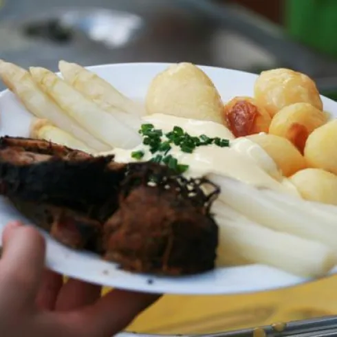 Ein Teller mit gekochtem Spargel, Kartoffeln und einem Stück Fleisch. Das Gericht ist mit Sauce und frischem Schnittlauch garniert.