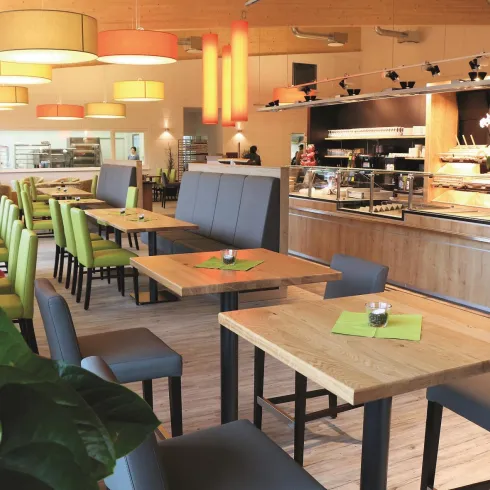 Ein modernes Restaurant mit hellen Farben und gemütlichen Tischen. Die Einrichtung ist einladend und bietet Platz für viele Gäste.