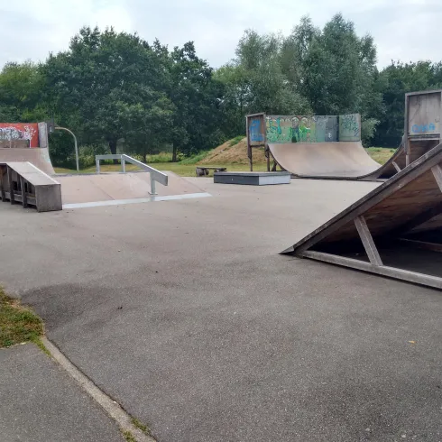 Ein Skatepark mit verschiedenen Rampen und flachen Flächen. Der Platz ist grün umgeben und bietet Platz zum Skaten und Üben.
