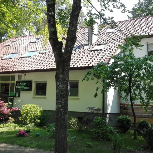 Ein modernes Gebäude umgeben von Bäumen und Pflanzen. Der Eingang ist barrierefrei gestaltet.