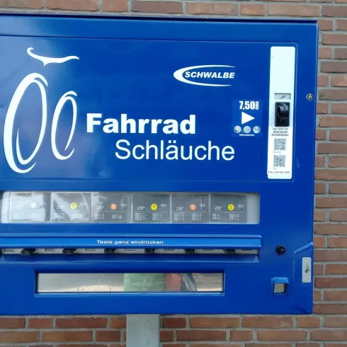 Ein blauer Automat zum Verkauf von Fahrradschläuchen. Er ist gut sichtbar an einer Ziegelwand platziert.