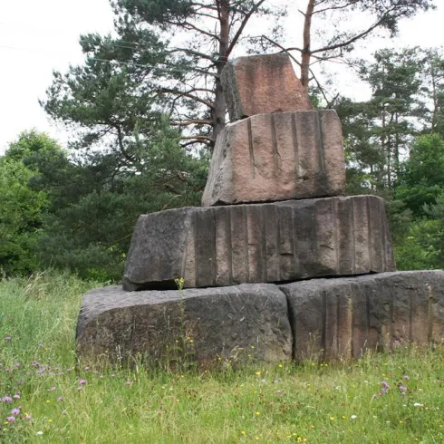 Ein stabiles Steinhaufen inmitten von grüner Wiese und Bäumen. Die Natur umrahmt die monumentale Struktur.
