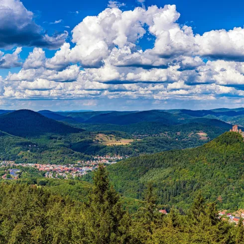 Eine herrliche Aussicht auf eine grüne Landschaft mit Hügeln und einem Schloss in der Ferne. Der Himmel ist blau mit vielen weißen Wolken.