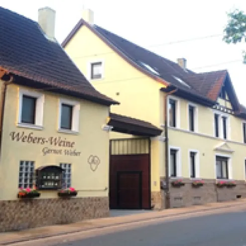 Ein charmantes, gelbes Gebäude mit dem Schriftzug "Webers-Weine". Es zeigt eine ländliche Weinstube mit Fensterblumen.