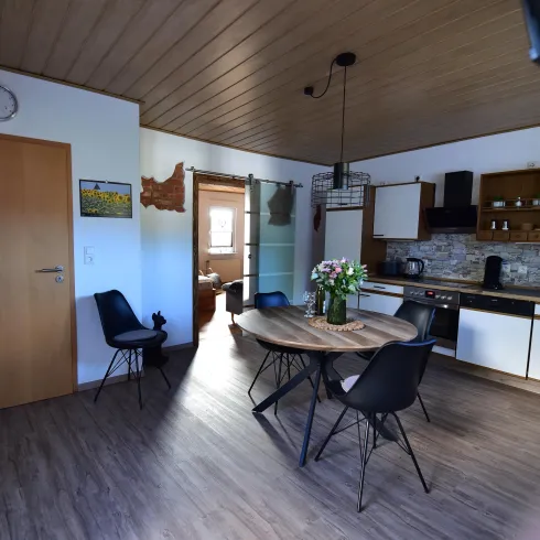 Eine moderne Küche mit einem runden Esstisch und schwarzen Stühlen. Die Wände sind hell, und es gibt große Fenster, die viel Licht hereinlassen.