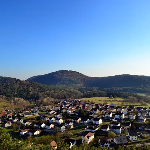 Ein malerisches Dorf in einer grünen Landschaft mit Hügeln im Hintergrund. Der blaue Himmel sorgt für eine friedliche Atmosphäre.