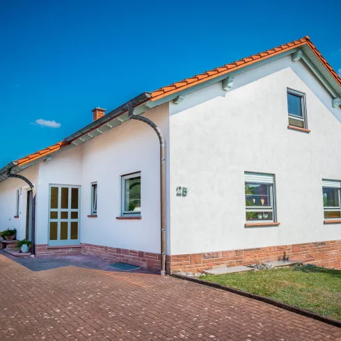 Ein modernes Einfamilienhaus mit rotem Dach und weißen Wänden. Der Garten ist gepflegt und das Ambiente ist freundlich und einladend.