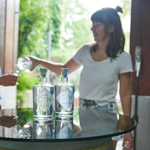 Zwei Frauen stehen an einem Tisch mit Flaschen Gin. Eine Frau gießt ein Getränk in ein Glas.