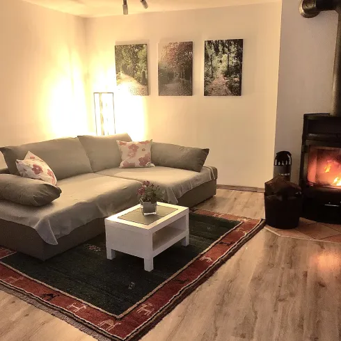Ein gemütlicher Wohnraum mit einem grauen Sofa und einem kleinen weißen Tisch. Neben dem Sofa steht ein Kamin, der eine warme Atmosphäre schafft.
