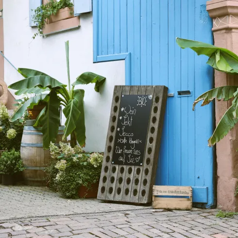 Ein schönes Café mit einer blauen Tür und einer Tafel im Freien. Banane und andere Pflanzen schmücken den Eingang.