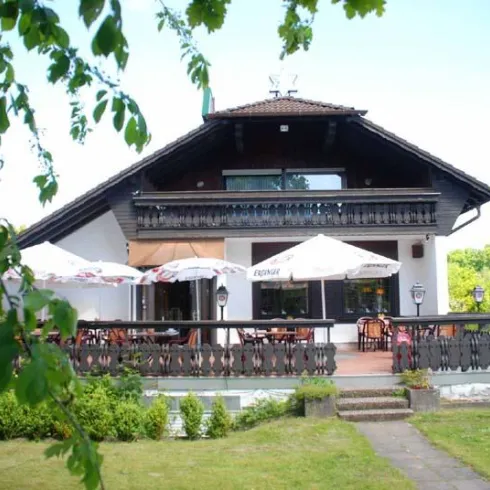 Ein charmantes Haus mit einem großen Balkon und mehreren Sonnenschirmen. Der Garten ist grün und einladend.