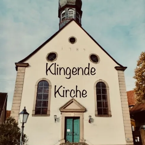 Eine historische Kirche mit einem markanten Turm und einem einladenden Eingang. Der Schriftzug "Klingende Kirche" ist prominent auf der Fassade zu sehen.