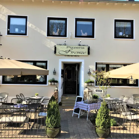 Ein einladendes Restaurant mit einem Außenbereich, der mit Tischen und Sonnenschirmen ausgestattet ist. Die Fassade des Gebäudes ist hell und freundlich gestaltet.