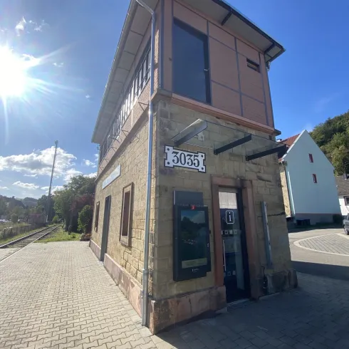 Ein modernes Gebäude mit einer Kombination aus Stein und Holz. Es befindet sich an einer Straße und ist von grüner Natur umgeben.