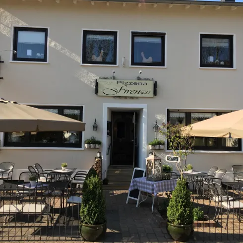 Ein gemütliches Restaurant mit dem Namen "Pizzeria Finesse". Es gibt einen Außenbereich mit Tischen, Sonnenschirmen und Pflanzen.