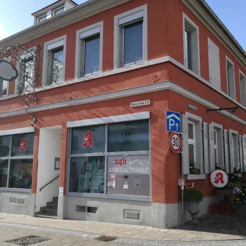 Ein rotes Gebäude mit großen Fenstern und einem Eingangsbereich. Vor dem Gebäude gibt es Parkplätze und Fahrräder.