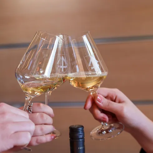 Drei Gläser mit weißem Wein stoßen an. Im Hintergrund ist eine unauffällige Holzoberfläche zu sehen.