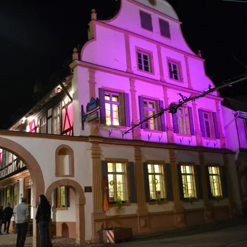 Ein historisches Gebäude mit bunten Lichtern in der Nacht. Menschen spazieren in der Nähe und genießen die Atmosphäre.