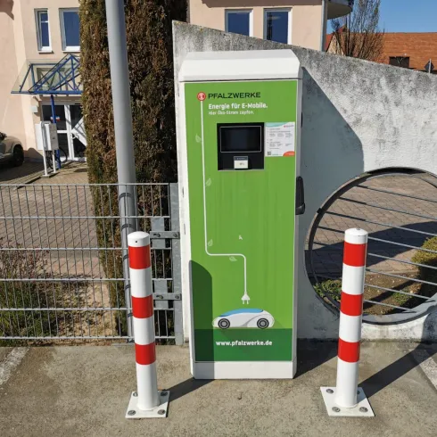 Eine Ladestation für Elektroautos in einem Wohngebiet. Sie ist grün und zeigt ein Symbol für das Aufladen von Fahrzeugen.