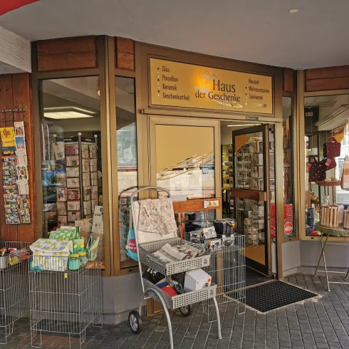 Ein einladender Laden mit einer großen Glasfront und einem weißen Schild. Vor der Tür stehen Einkaufskörbe und der Eingangsbereich ist freundlich gestaltet.