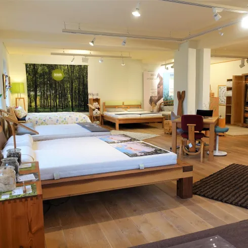 Ein modernes Schlafzimmergeschäft mit verschiedenen Betten und Matratzen. Die Einrichtung ist freundlich und einladend, mit viel natürlichem Holz.