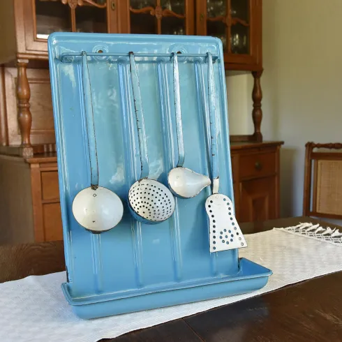 Ein blauer Küchenutensilienhalter mit drei verschiedenen Löffeln. Der Halter steht auf einem Tisch in einem hellen Raum.