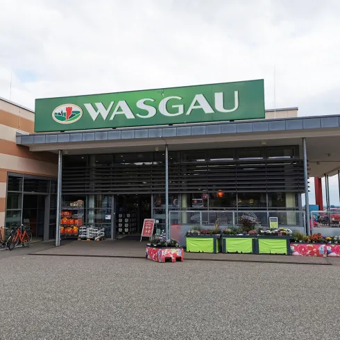 Ein Supermarkt mit der Aufschrift "WASGAU". Vor dem Eingang sind Blumen und Fahrräder zu sehen.