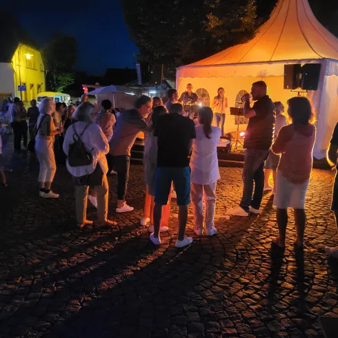 Eine festliche Veranstaltung bei Nacht mit einer Band, die spielt. Menschen versammeln sich, um die Musik zu genießen und zu tanzen.