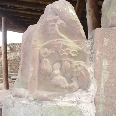 Eine alte Steinmetzarbeit mit kunstvollen Schnitzereien, die Pflanzen und Tiere darstellen. Die Skulptur befindet sich in einem archäologischen Bereich.