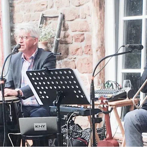 Zwei Musiker spielen live auf einer Bühne im Freien. Der Sänger ist am Mikrofon, während der Trompeter sein Instrument spielt.