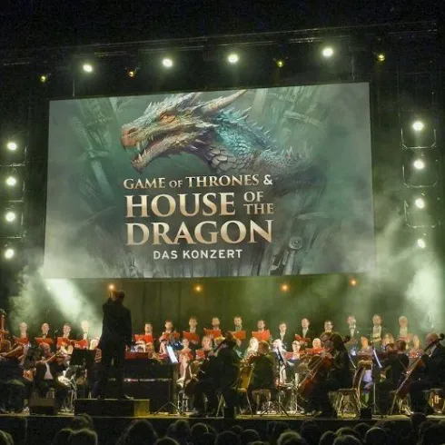 Ein Orchester führt ein Konzert zu "Game of Thrones" und "House of the Dragon" auf. Im Hintergrund sieht man eine große Leinwand mit einem Drachenmotiv.