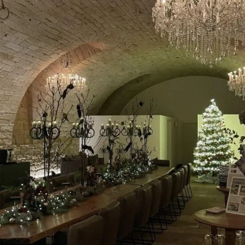 Ein festlich dekorierter Raum mit einem Weihnachtsbaum und eleganten Kristallleuchtern. Der Tisch ist mit Lichtern und Pflanzen geschmückt.