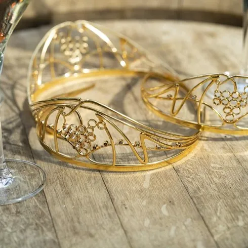 Zwei elegante, goldene Haarschmuckstücke liegen auf einem Holztablett. Im Hintergrund stehen Gläser mit Schaumwein.