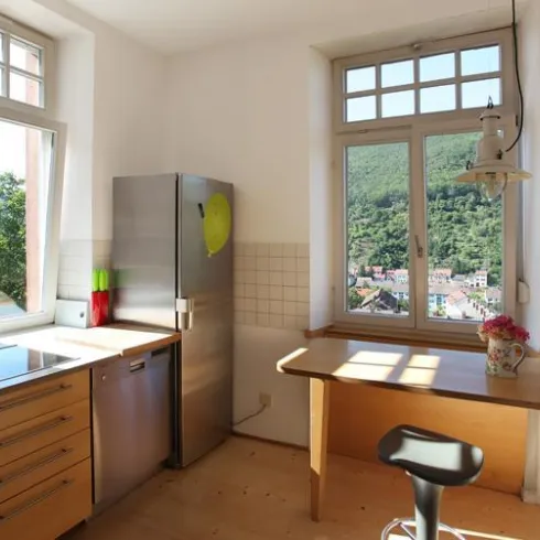 Eine helle Küche mit modernen Möbeln und großen Fenstern. Durch die Fenster ist eine schöne Aussicht auf die umliegende Natur zu sehen.