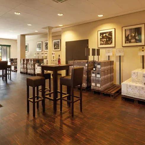 Ein einladender Verkaufsraum mit Holzfußboden und hohen Tischen. Regale mit Weinflaschen und Fotografien an den Wänden schaffen eine angenehme Atmosphäre.