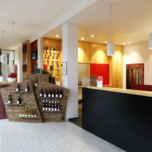 Ein heller Empfangsbereich mit einem modernen Design. An der Wand sind Weinflaschen ausgestellt, und es gibt einen Bartresen aus Holz.