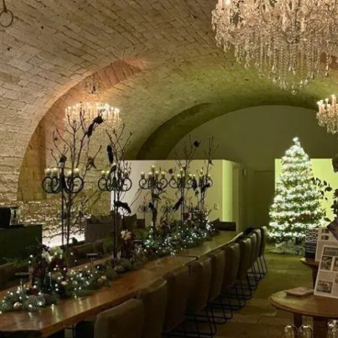 Ein festlich dekorierter Raum mit einem großen Tisch und eleganten Stühlen. In der Ecke steht ein geschmückter Weihnachtsbaum und der Raum ist mit Kronleuchtern beleuchtet.