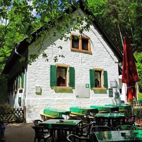 Ein hübsches Haus im Wald mit grünen Fensterläden. Draußen stehen Tische und Stühle für Gäste.