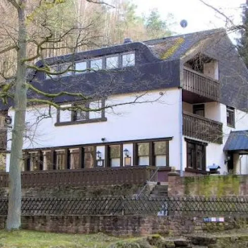 Ein modernes Haus mit mehreren Balkonen, umgeben von Bäumen. Es hat große Fenster und befindet sich in einer ruhigen, naturnahen Umgebung.