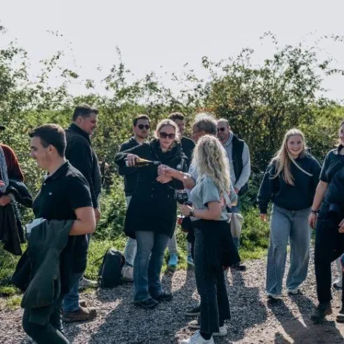 Eine Gruppe von Menschen steht im Freien und unterhält sich. Die Umgebung ist grün und hell erleuchtet von der Sonne.