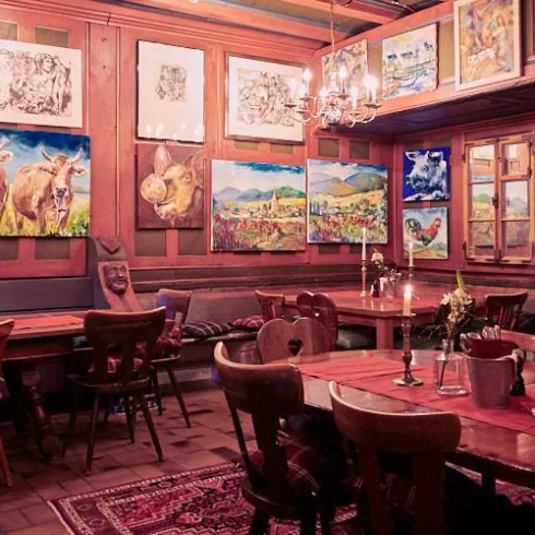 Ein gemütliches Restaurant mit Holzmöbeln und bunten Gemälden an den Wänden. Der Raum ist warm beleuchtet und lädt zum Verweilen ein.