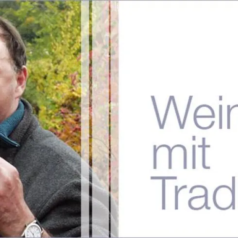Ein Winzer steht in einem Weinberg und hält Trauben in der Hand. Die Umgebung zeigt grüne Weinreben und die Botschaft betont Tradition im Weinbau.