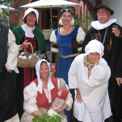 Eine Gruppe von Personen in historischer Kleidung steht zusammen. Sie tragen verschiedene Kostüme aus vergangenen Zeiten und lächeln in die Kamera.