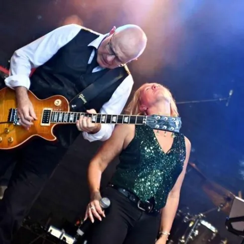 Ein Musiker spielt Gitarre, während eine Sängerin auf der Bühne performt. Die Atmosphäre ist lebhaft und energiegeladen.