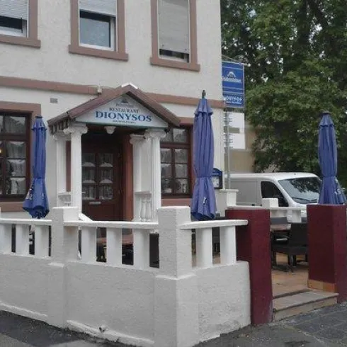 Ein Restaurant mit dem Namen "Dionysos" und einem einladenden Außenbereich. Es gibt blaue Sonnenschirme und Tischstühle vor dem Eingang.