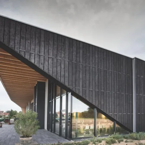 Ein modernes Gebäude mit schrägen Dachlinien und Holzverkleidung. Die große Fensterfront bietet viel Licht und eine einladende Atmosphäre.
