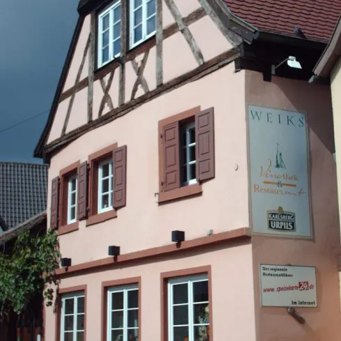 Ein charmantes, zweigeschossiges Haus mit einem rosa Putz und einem gefliesten Dach. An der Fassade befindet sich eine Werbetafel für ein Restaurant.
