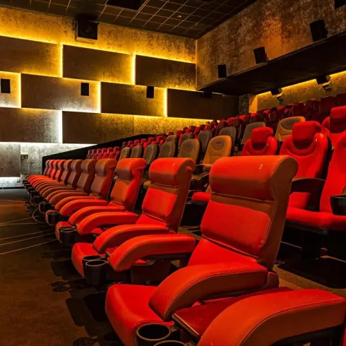 Ein modernes Kino mit roten, bequemen Sitzen und gedämpfter Beleuchtung. Die Plätze sind leer und die Atmosphäre ist einladend.